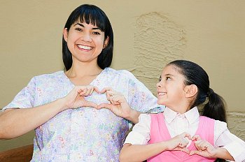 Mother and daughter make hand hearts over their hearts