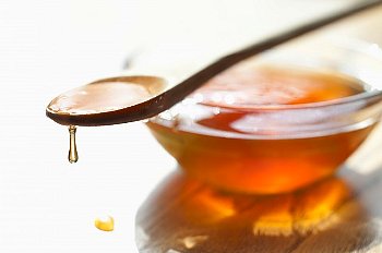 A spoon full of honey sits on a bowl full of honey