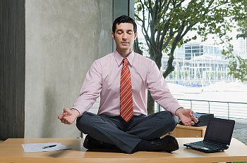 A man meditating in an office, on top of his desk