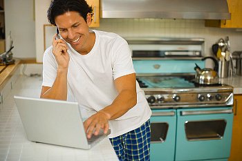 A man wearing pajamas while using his laptop in the kitchen