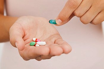A woman holds a selection of pills in her hand and holds out a blue pill with the other