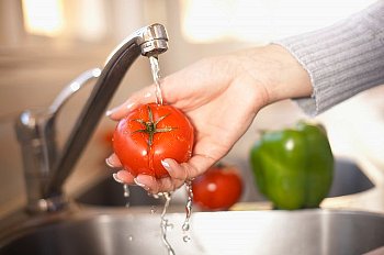 Woman washes a tomato in the sink