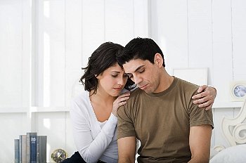 Distressed couple sit holding each other