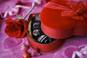 A red box of Valentine's Day chocolate, sitting beside a red rose