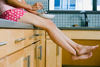A woman eating from a bowl while sitting on her kitchen countertop