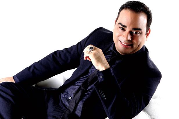 Gilberto Santa Rosa sitting on a chair in a black suit
