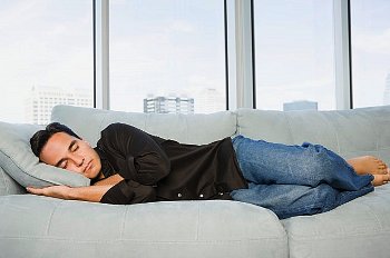 Man in a dark shirt and jeans sleeps on a couch