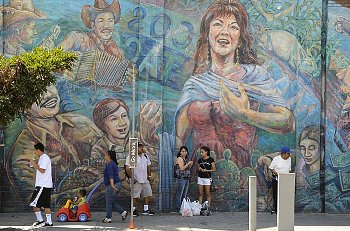 People stand in front of a large neighborhood mural of a people