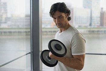 Man standing and looking down as his lifts a dumbbell with his right arm