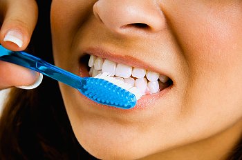 A woman brushes her teeth with a blue tooth brush