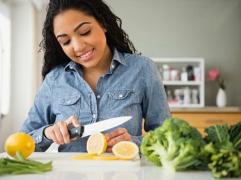 A woman is cutting a lemon on a table with broccoli