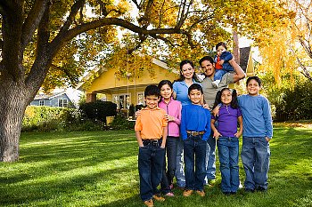 Large family stands in front yard under a tree.