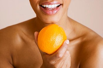 A woman holds an orange in front of her face