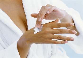 Woman in a white bathrobe applying moisturizer to her hand