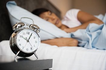 Alarm clock sits on a bed side table as woman sleeps