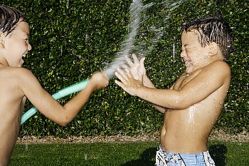 Little boys wet each other with a hose