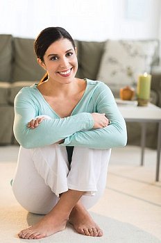 Woman sits on floor at home relaxed and smiling