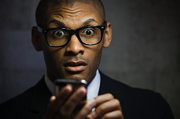 Man in a suit looks shocked while holding a cell phone