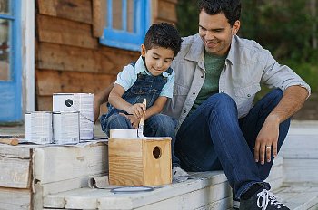 Father and son sit on the front stoop and paint a bird house