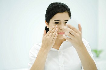 Girl in white touching eye and looking into mirror