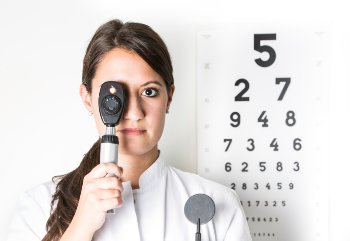 An optometrist holding retinascope in front of eye chart