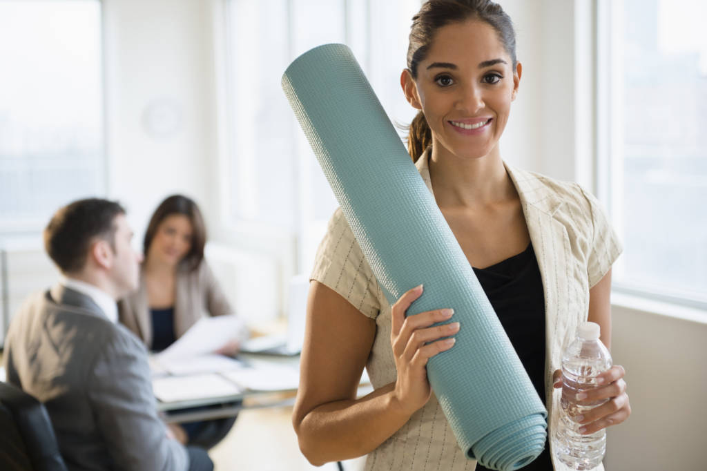 A businesswoman holding a yoga mat and a bottle of water in her office