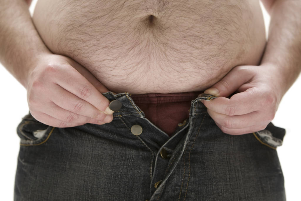 A man with a large belly trying to button his jeans