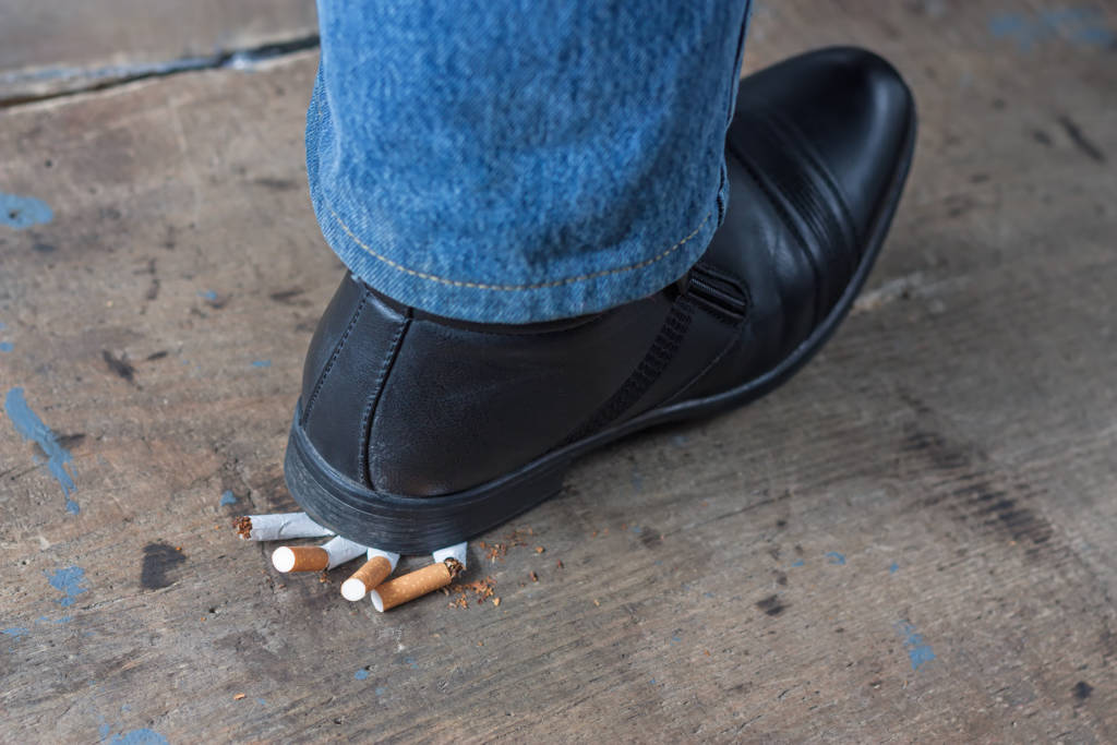 man quitting smoking, foot on cigarettes